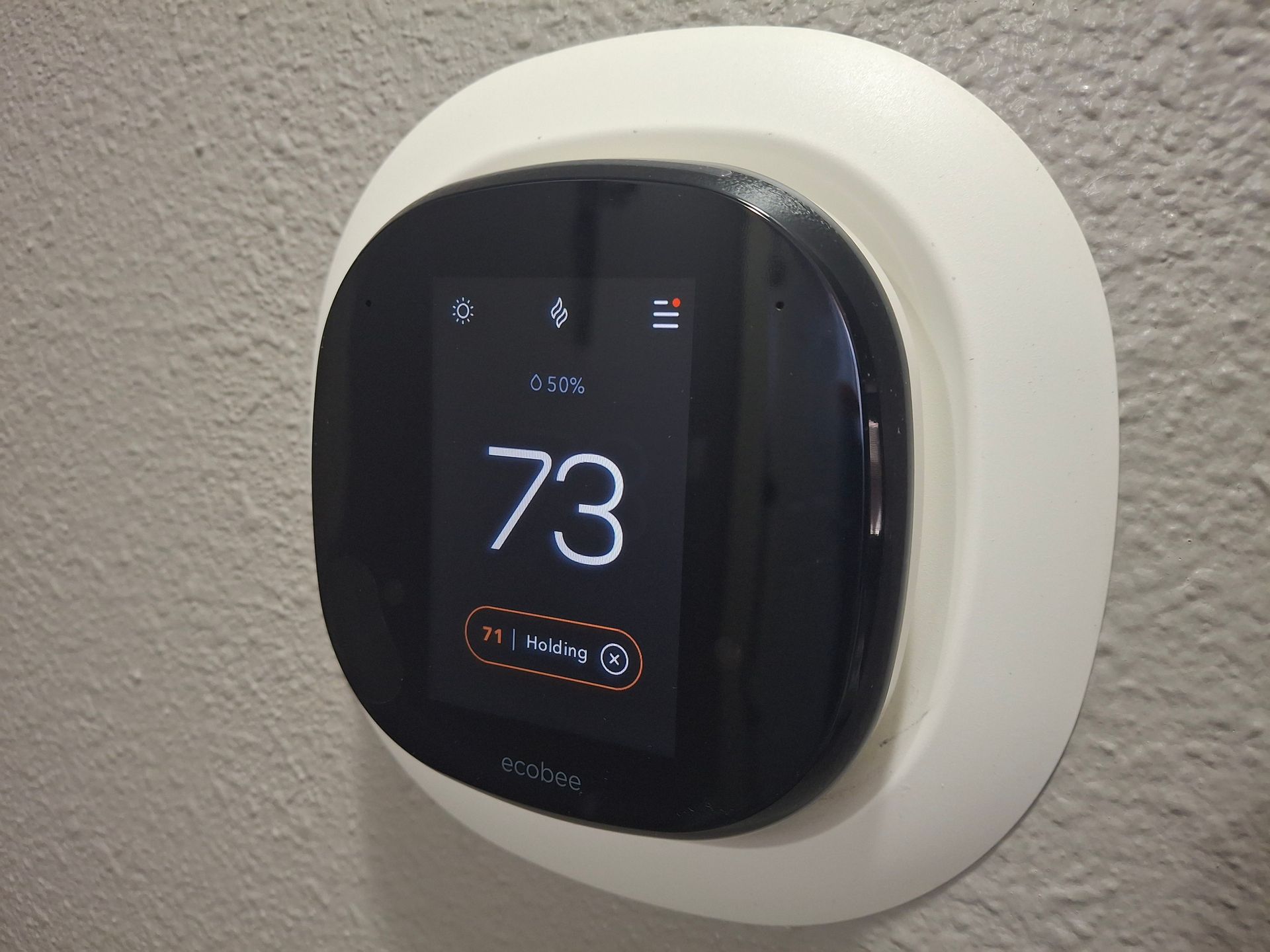 Wall-mounted smart thermostat displaying 73°F on a white wall