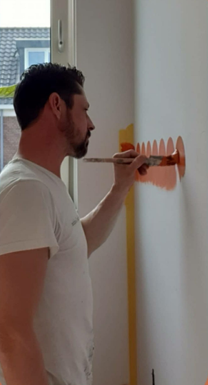 Stefan Godrie schildert een lambrisering met een oranje kwast en verf.