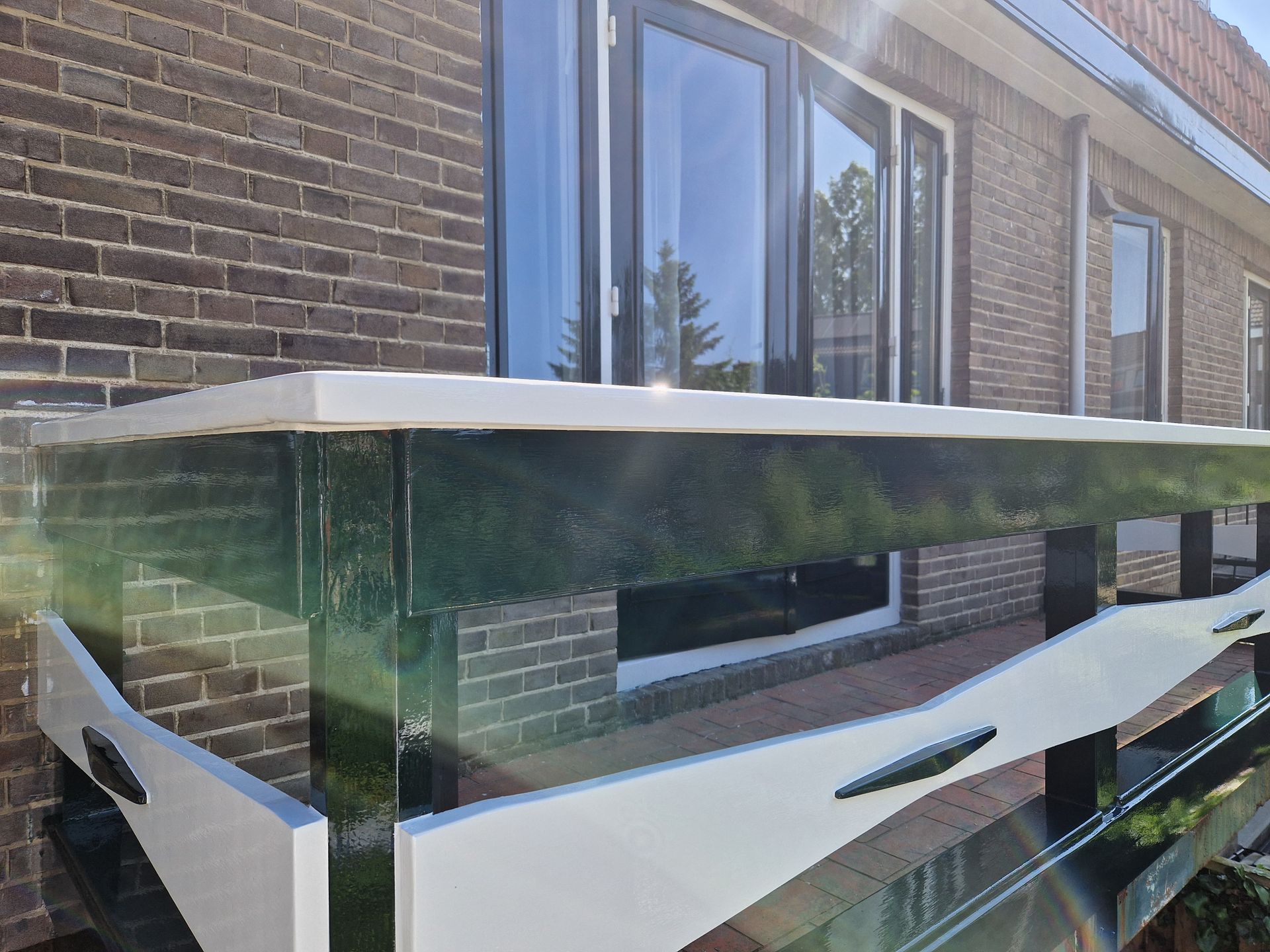 Balkon met witte balustrade, groene afwerking, bakstenen muur, glanzende deuren.
