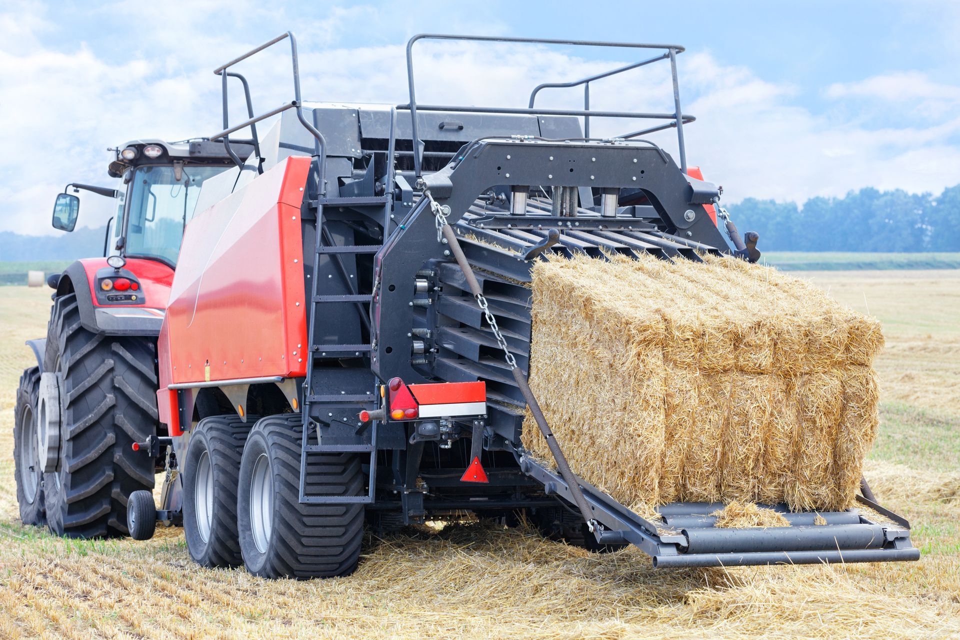 A tractor forms sheaves of straw into dense briquettes in a wheat field.