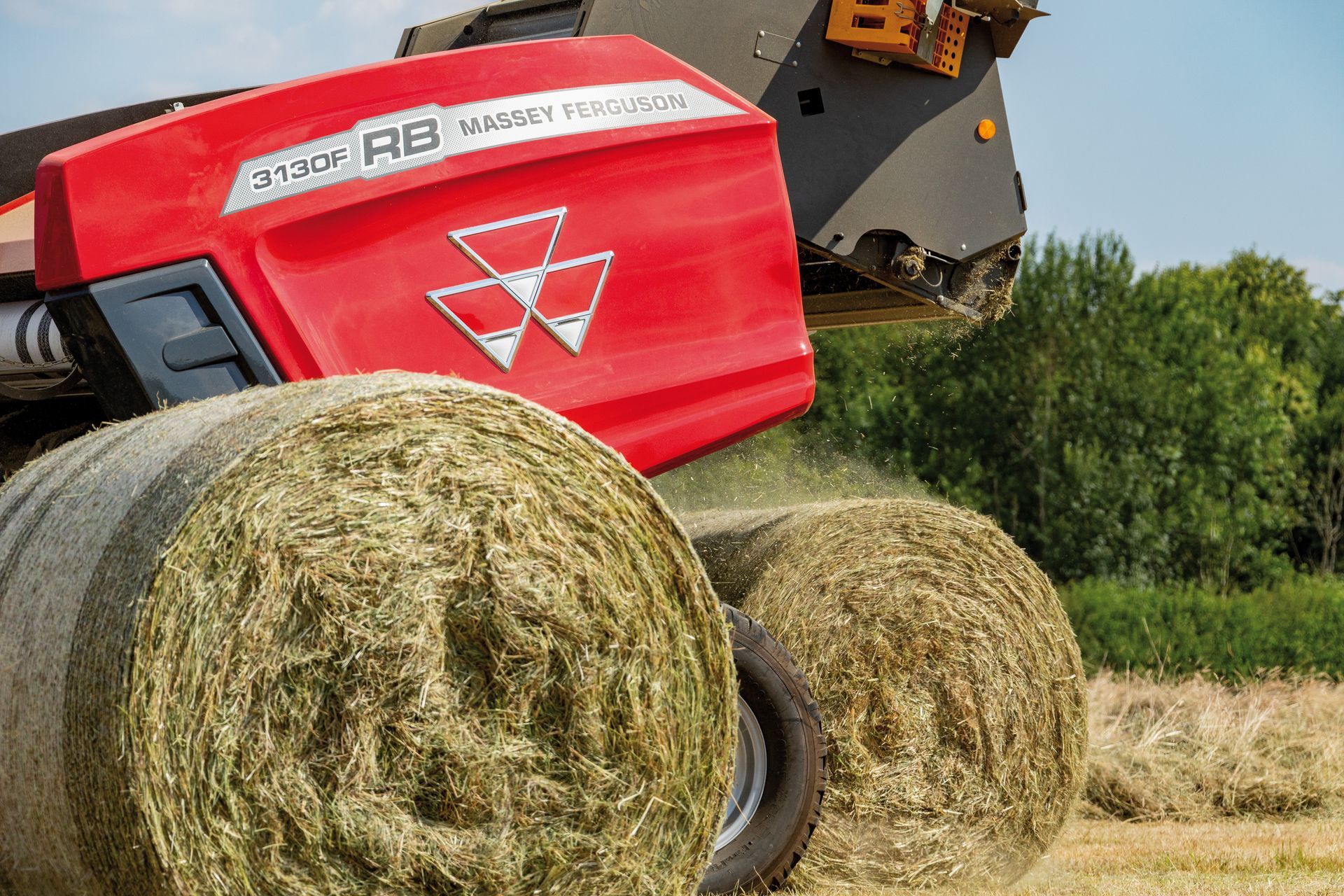 Red Massey Ferguson baler forming round hay bales in a field.
