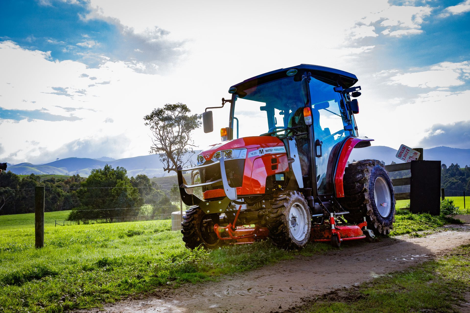A blue tractor with a trailer is parked in a field at sunset.