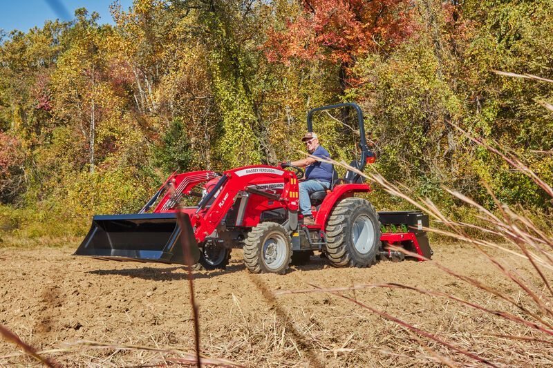 A mechanic performs farm equipment repairs and servicing on a blue tractor.