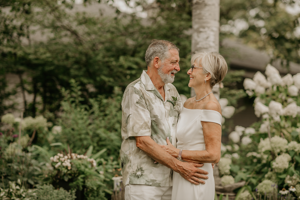 Older couple embracing in a lush garden, smiling at each other in soft light