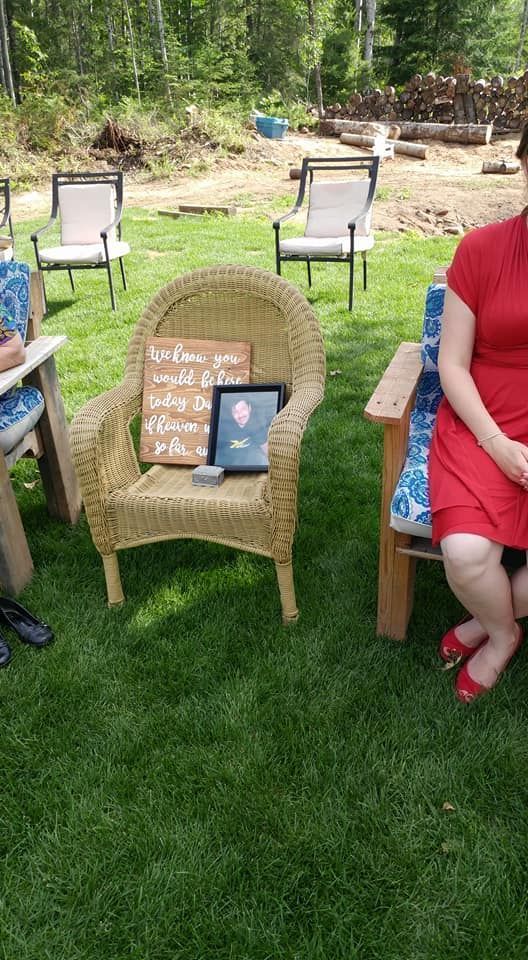 Outdoor lawn setup with wicker chairs, a decorative sign, and partially visible seated people at the sides