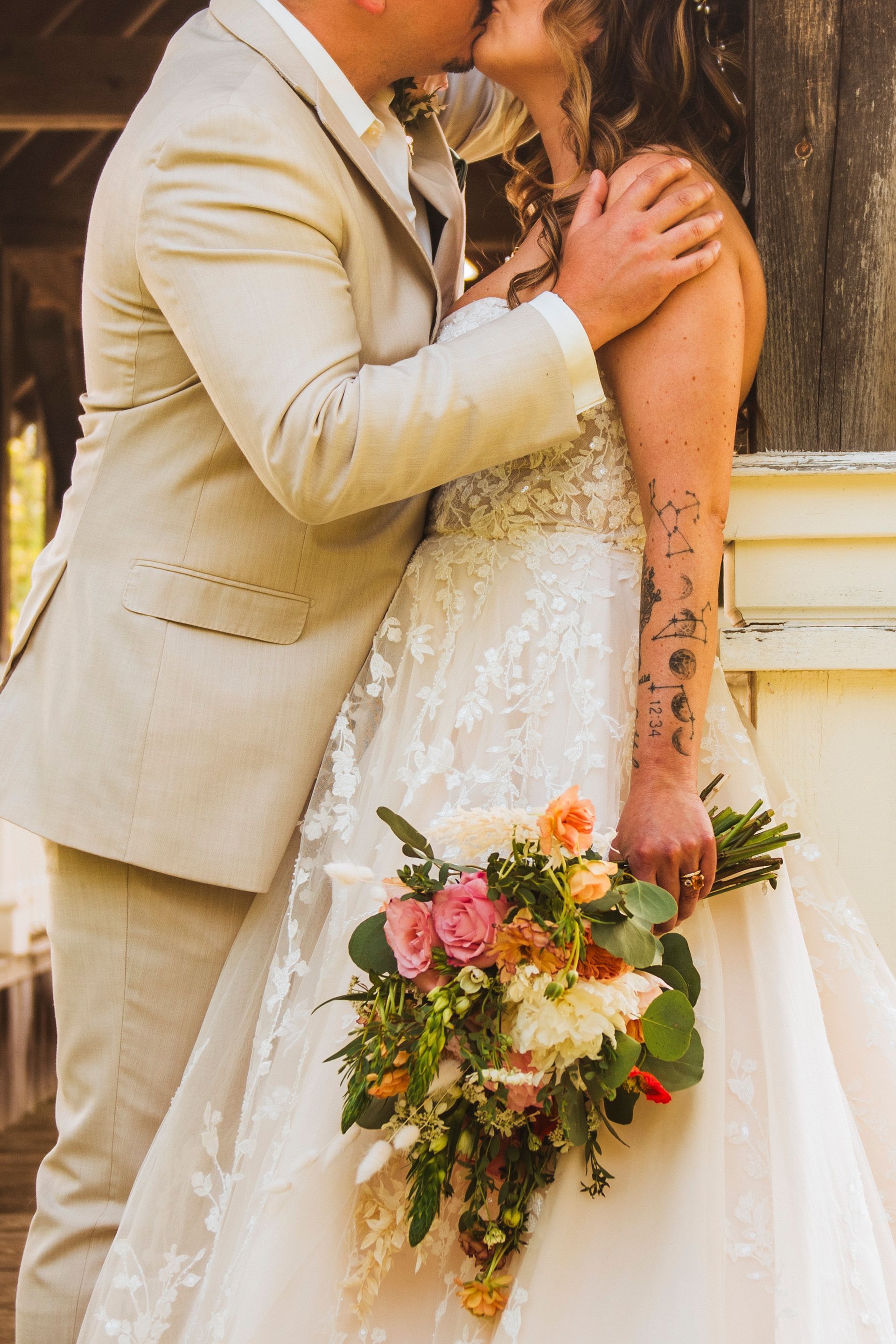 Bride and groom kissing, bride holding a cascading bouquet in a warm-toned wedding portrait