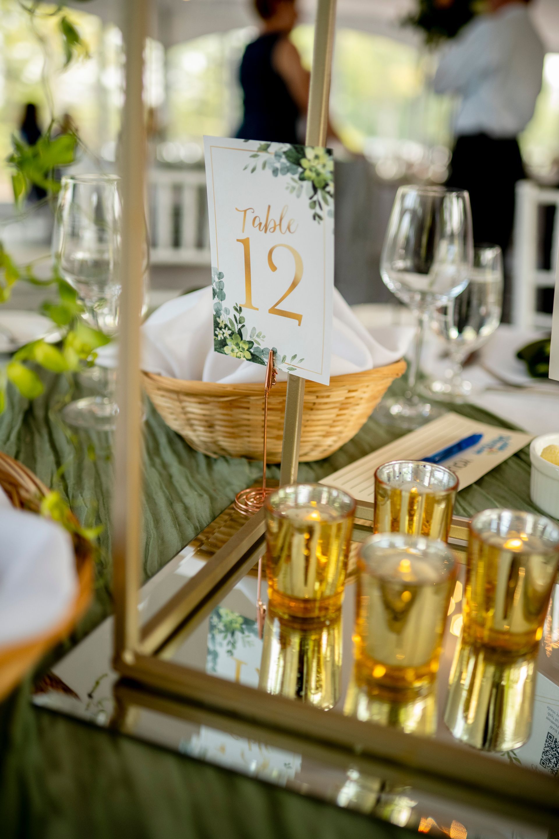 Table setting with gold glasses, a bread basket, and a place card marked 12 on a mirrored tray