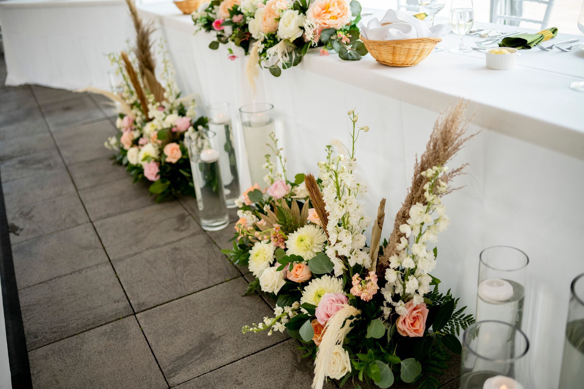 Floral arrangements with candles and lanterns decorating a white table at an indoor event