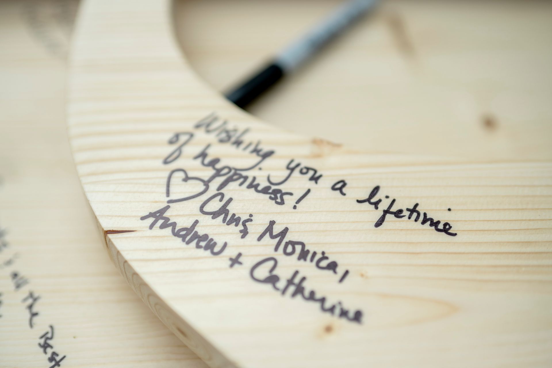 Handwritten names on a pale wooden table, with a pencil blurred in the background
