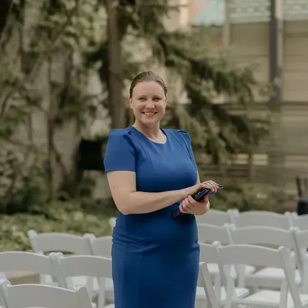 Woman in blue dress holding a remote, standing among white chairs outdoors
