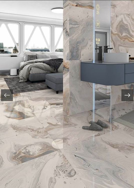 Camera da letto moderna con letto grigio, pavimento e pareti effetto marmo e un'elegante toeletta accanto a una finestra luminosa.