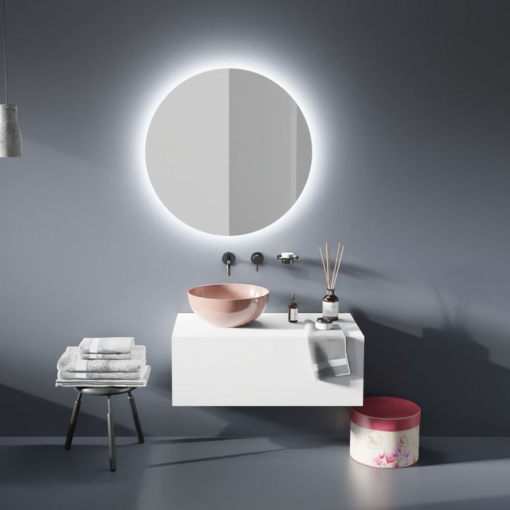 Mobile bagno moderno con specchio rotondo, lavabo rosa, mobiletto bianco, sgabello e accessori su una parete grigia.