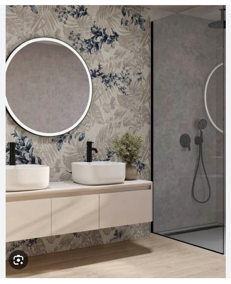 Bagno moderno con doppio lavabo, specchio rotondo, carta da parati floreale e cabina doccia.