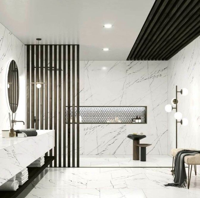 Bagno moderno in marmo bianco con dettagli neri, specchio rotondo, vasca freestanding, cabina doccia e lampade a sospensione.