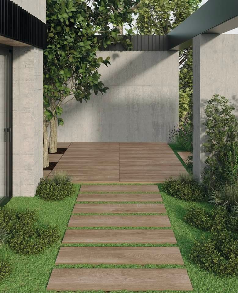 Cortile moderno con scalini in pietra, pavimentazione in legno e vegetazione tra muri in cemento.