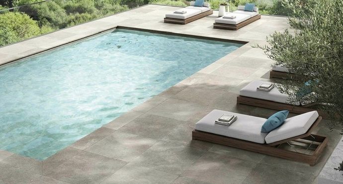 Moderna piscina nel cortile sul retro con patio in pietra chiara e lettini prendisole a bordo acqua.