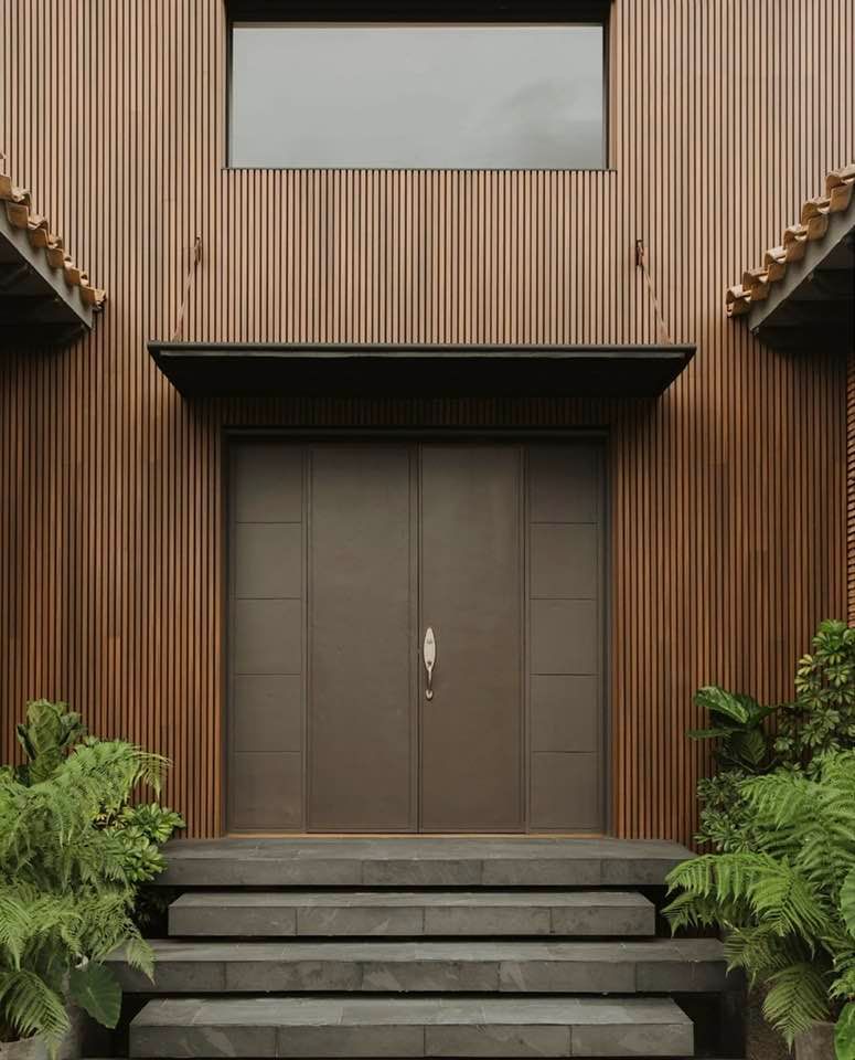 Ingresso moderno in legno con doppie porte, scalini e piante verdi su entrambi i lati.