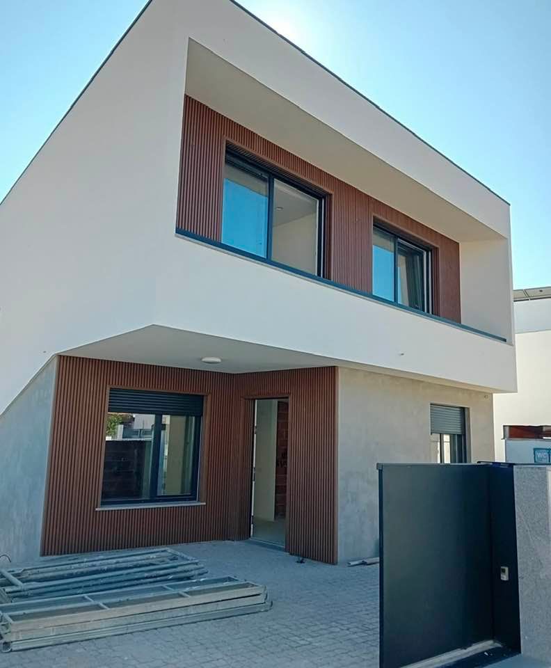 Casa moderna a due piani con dettagli in legno, ampie finestre e vialetto d'accesso con cancello, attualmente in costruzione.
