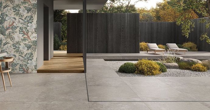 Patio moderno con pavimentazione in cemento, recinzione a doghe di legno scuro, sedie a sdraio e aiuole paesaggistiche.