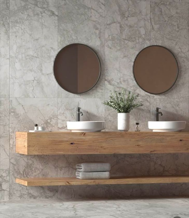Mobile bagno minimalista con ripiano in legno per il lavabo, specchi rotondi e decorazioni neutre su una parete grigia con texture.