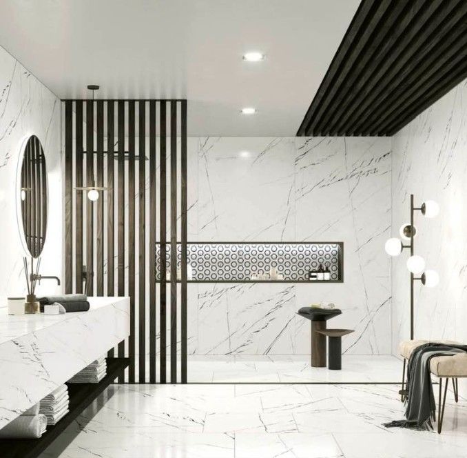Bagno moderno in marmo bianco con dettagli neri, vasca freestanding, specchio rotondo e applique a parete.