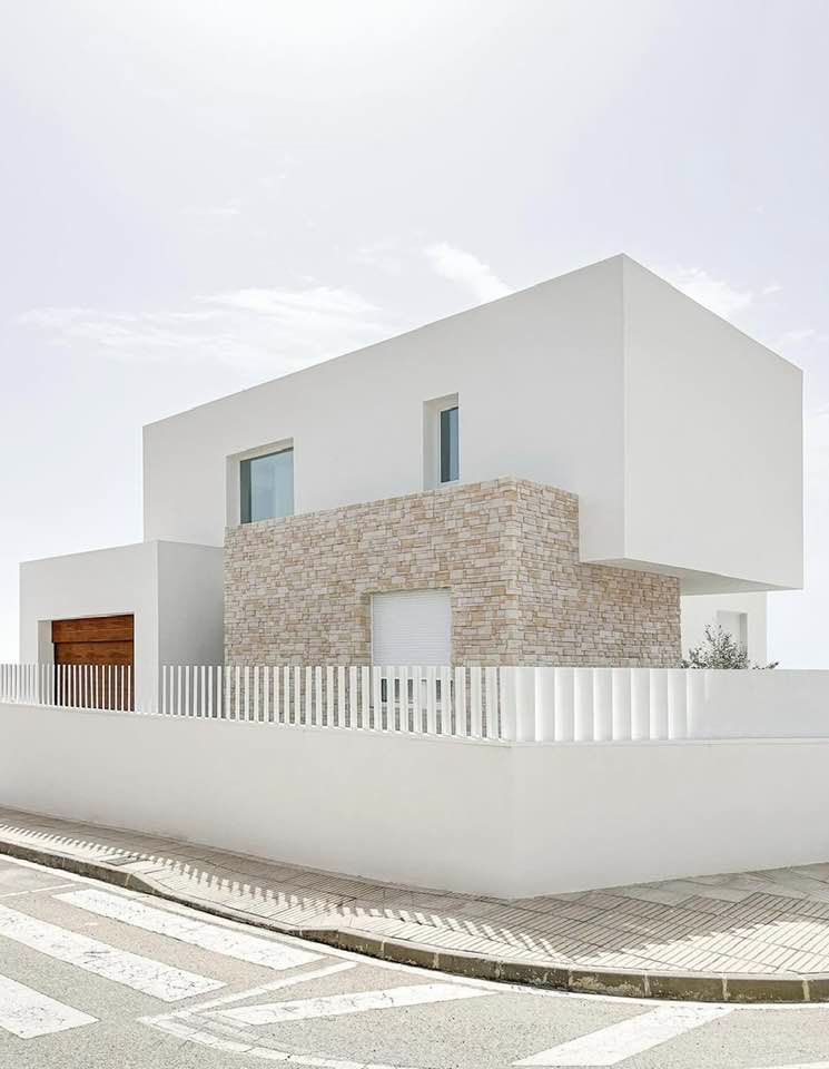 Casa moderna bianca con facciata in pietra, lotto d'angolo recintato e strada curva antistante