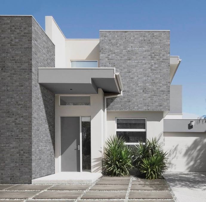 Esterno di una casa moderna, grigia e bianca, con porta d'ingresso, tenda da sole e piante del deserto.