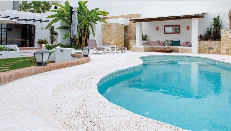 Moderno patio bianco con piscina turchese, palma, lettini e zona salotto con muretto in pietra.