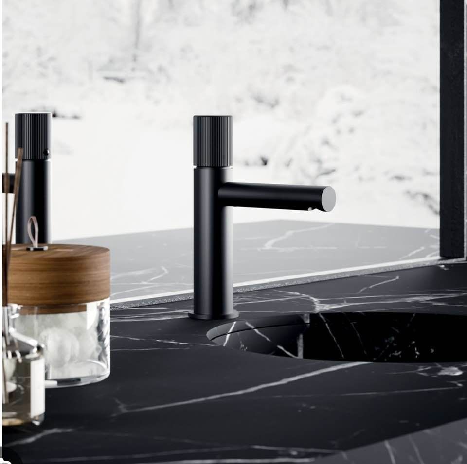 Rubinetto da bagno moderno di colore nero con dispenser di sapone integrato, installato su un piano lavabo in marmo nero.