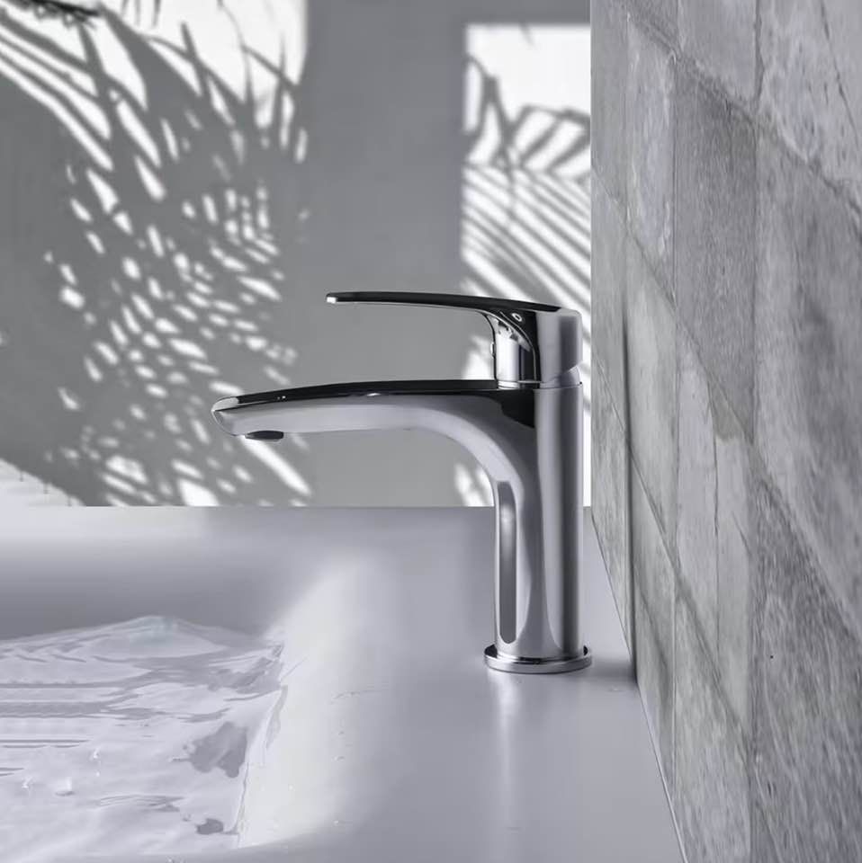 Rubinetto da bagno cromato accanto a un lavabo bianco, con motivi a foglie in ombra sulla parete.