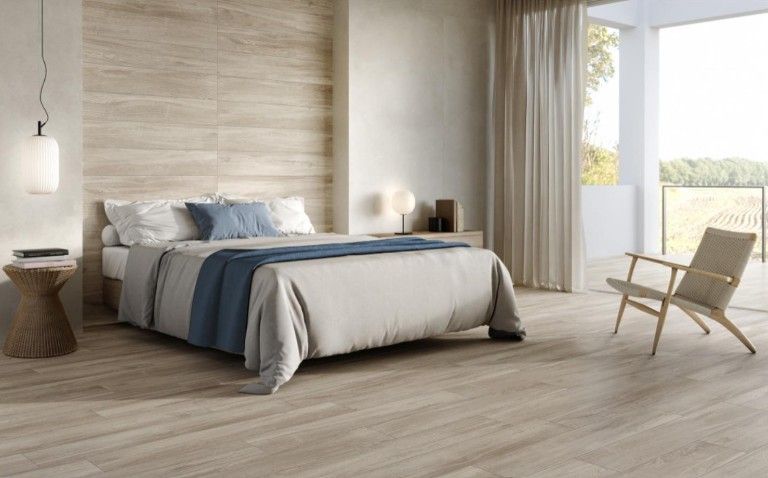 Camera da letto moderna con un letto ben rifatto, dettagli in legno e una poltrona accanto a grandi porte scorrevoli in vetro.
