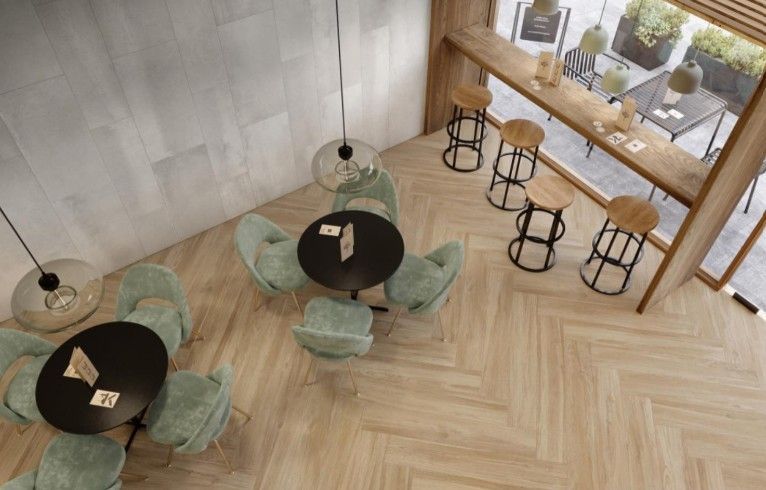 Caffè moderno con tavolini rotondi neri, sedie color menta e ampie vetrate che si affacciano su un pavimento in legno a spina di pesce.