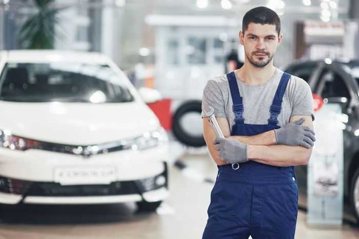 Een man in een overall staat voor een auto in een showroom.