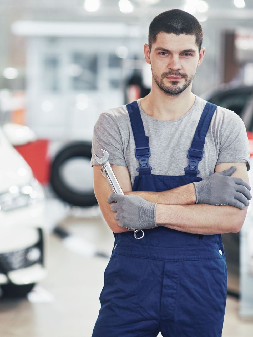 Een man in een overall houdt een moersleutel vast voor een auto.
