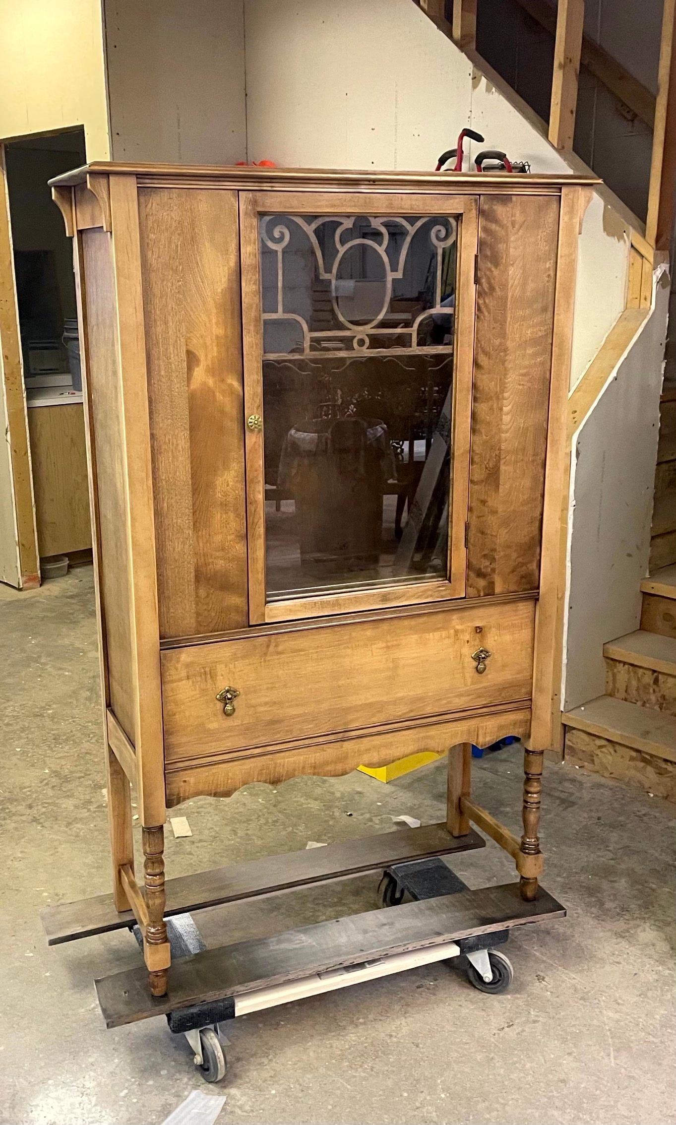 A wooden cabinet is sitting on a dolly in a room next to stairs.