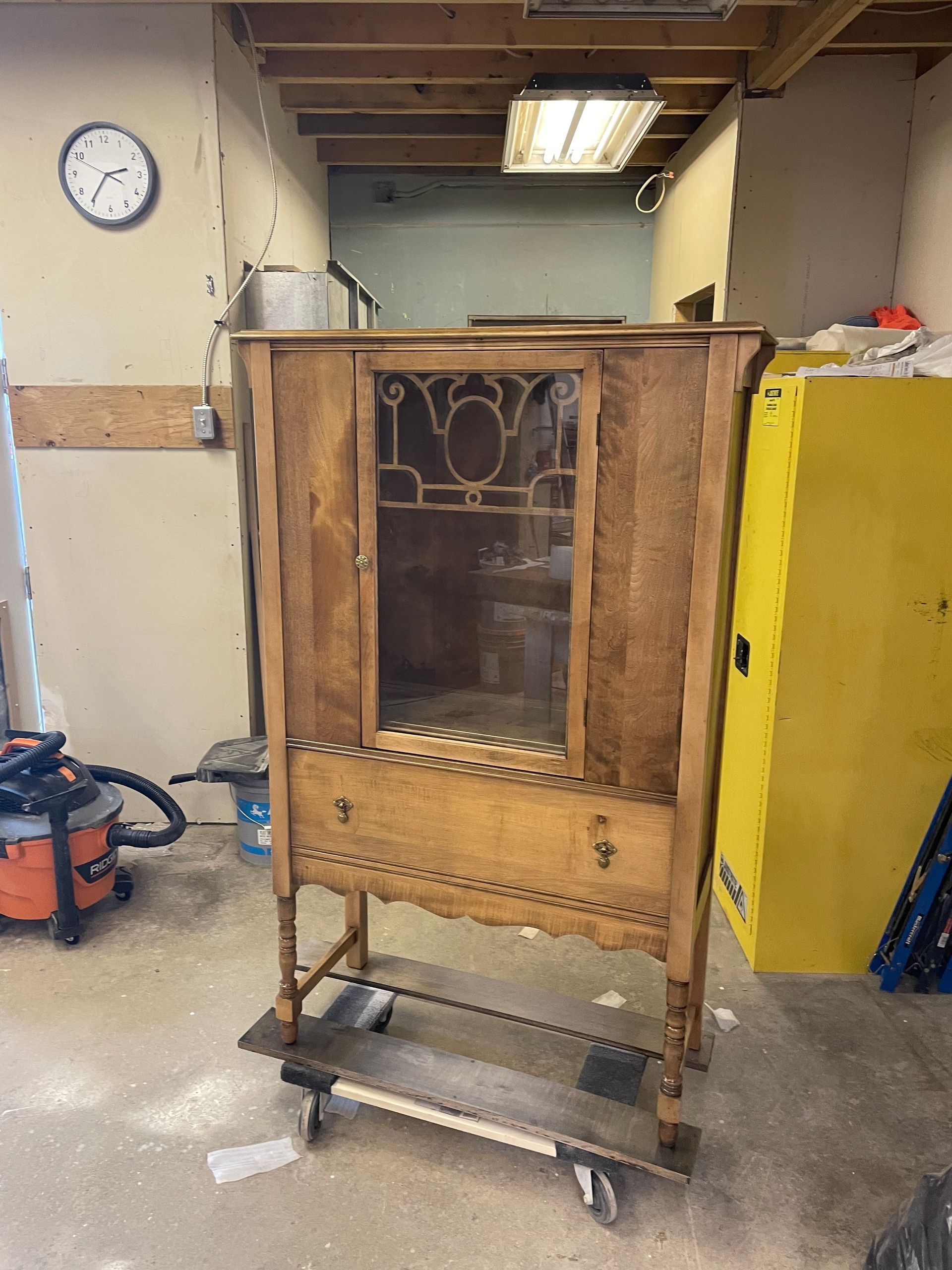 A wooden cabinet is sitting on a cart in a room with a clock on the wall.