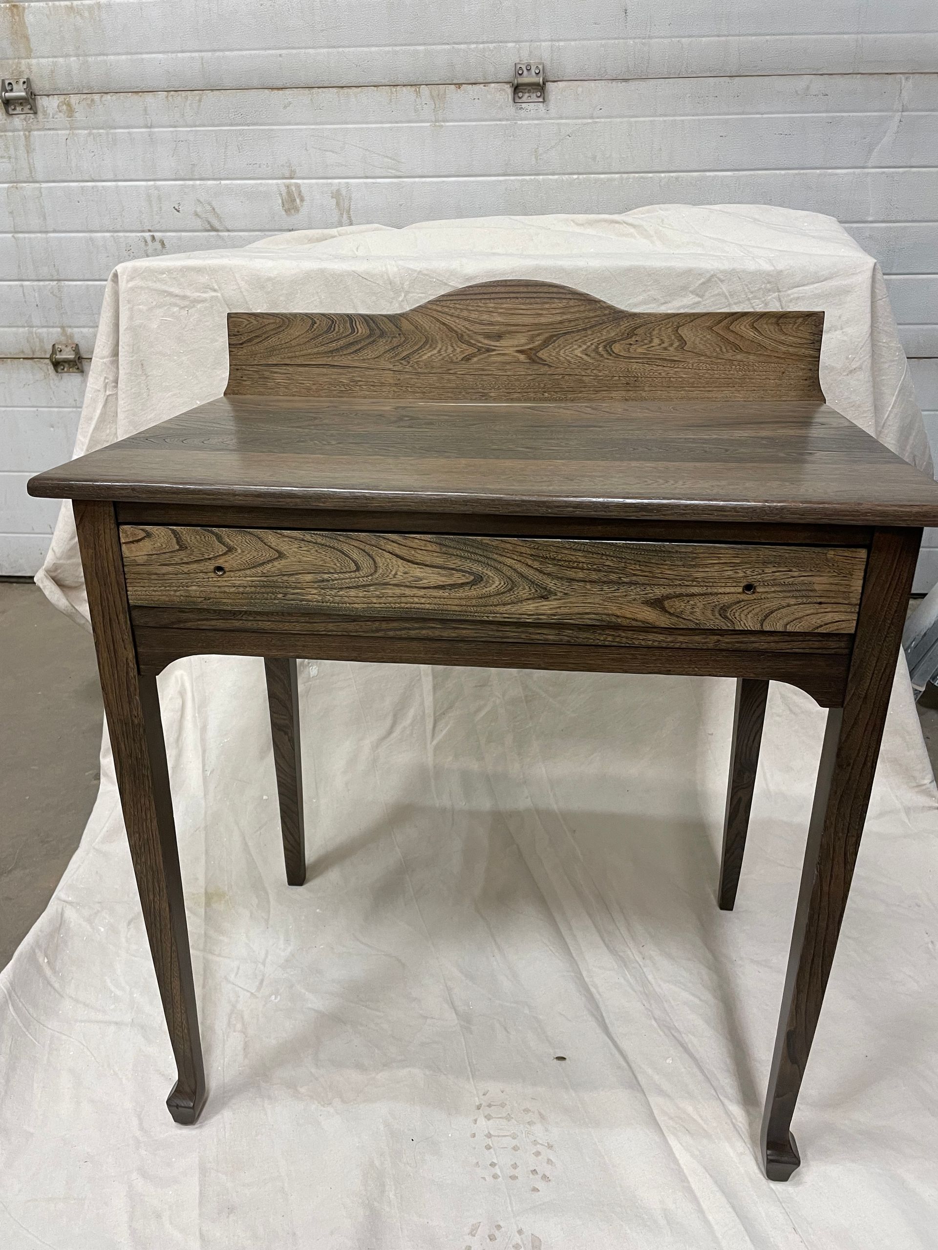 A small wooden table with a drawer is sitting on a white cloth.