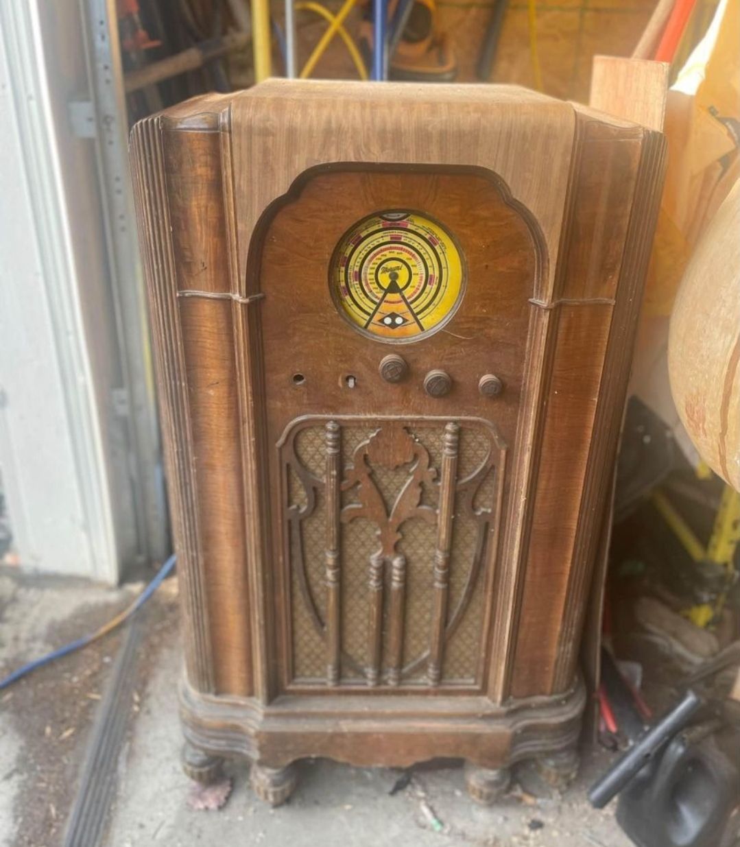 An old wooden radio is sitting on the ground in a garage.