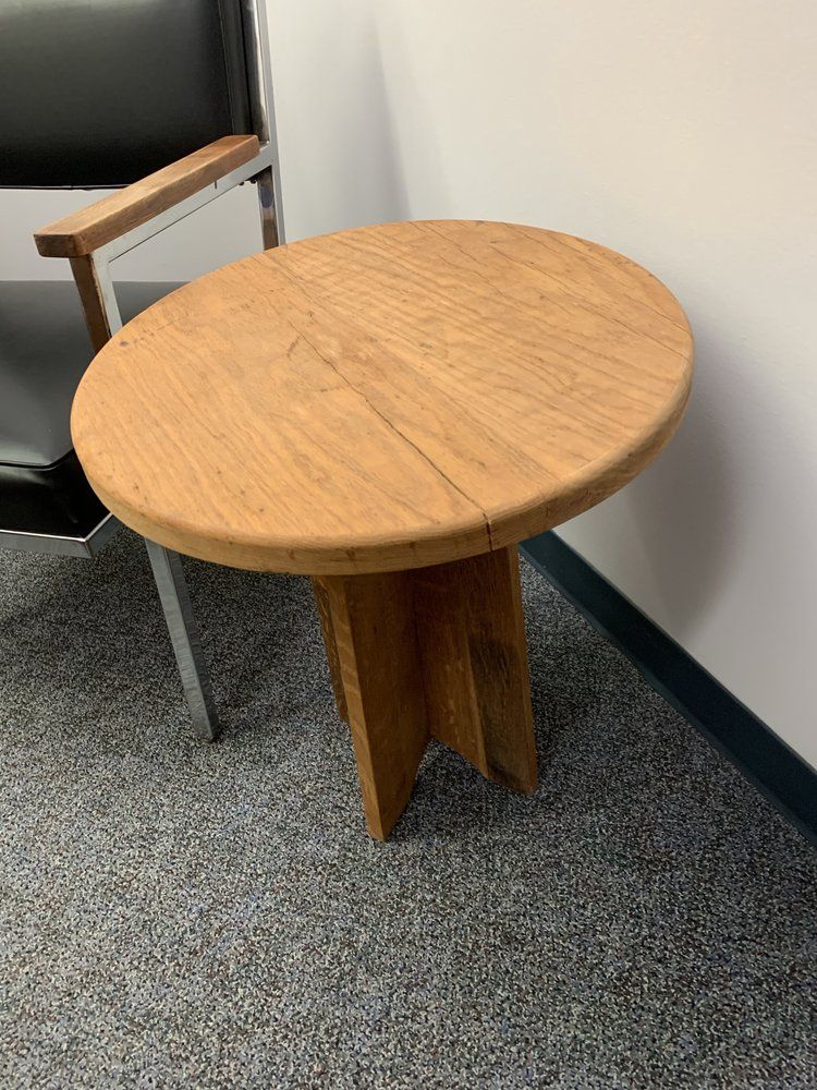 A round wooden table is sitting next to a chair in a room.
