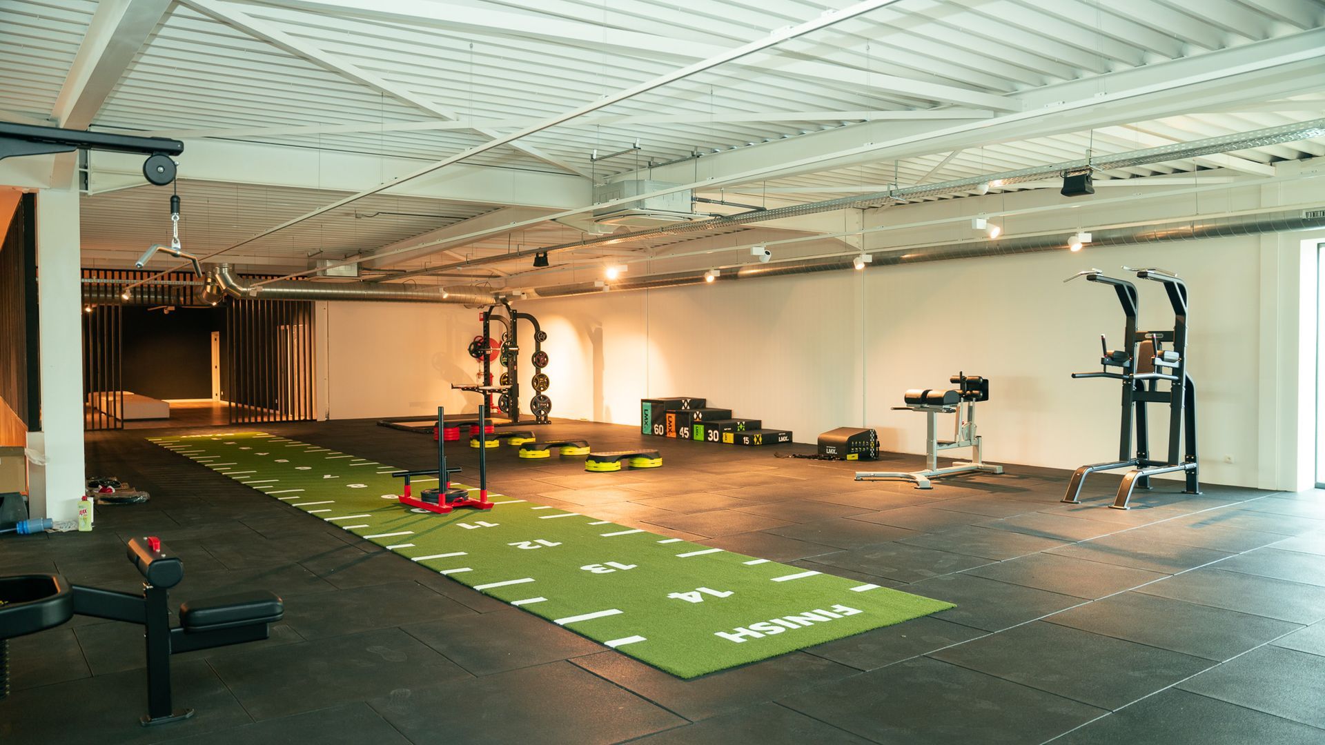 Een grote gymzaal met veel apparatuur en een groene mat op de vloer.