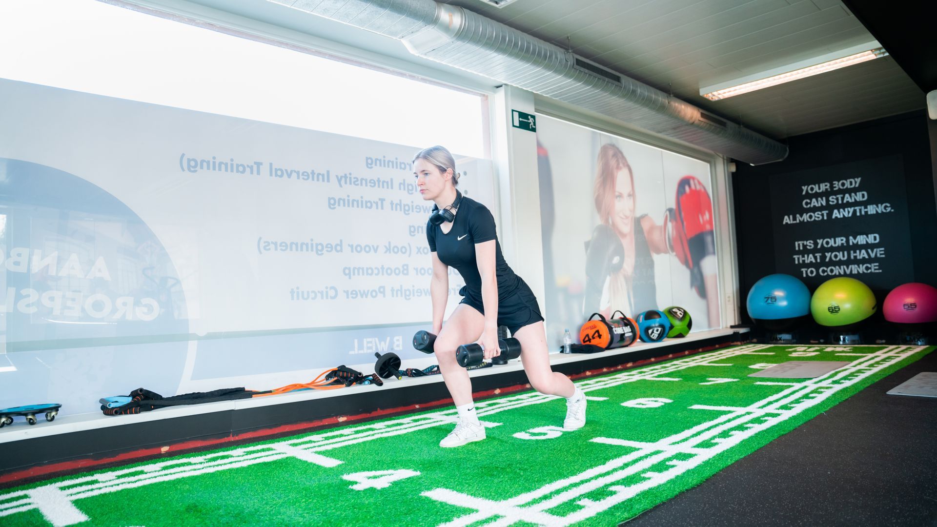 Een vrouw doet squats op een groene mat in een sportschool.