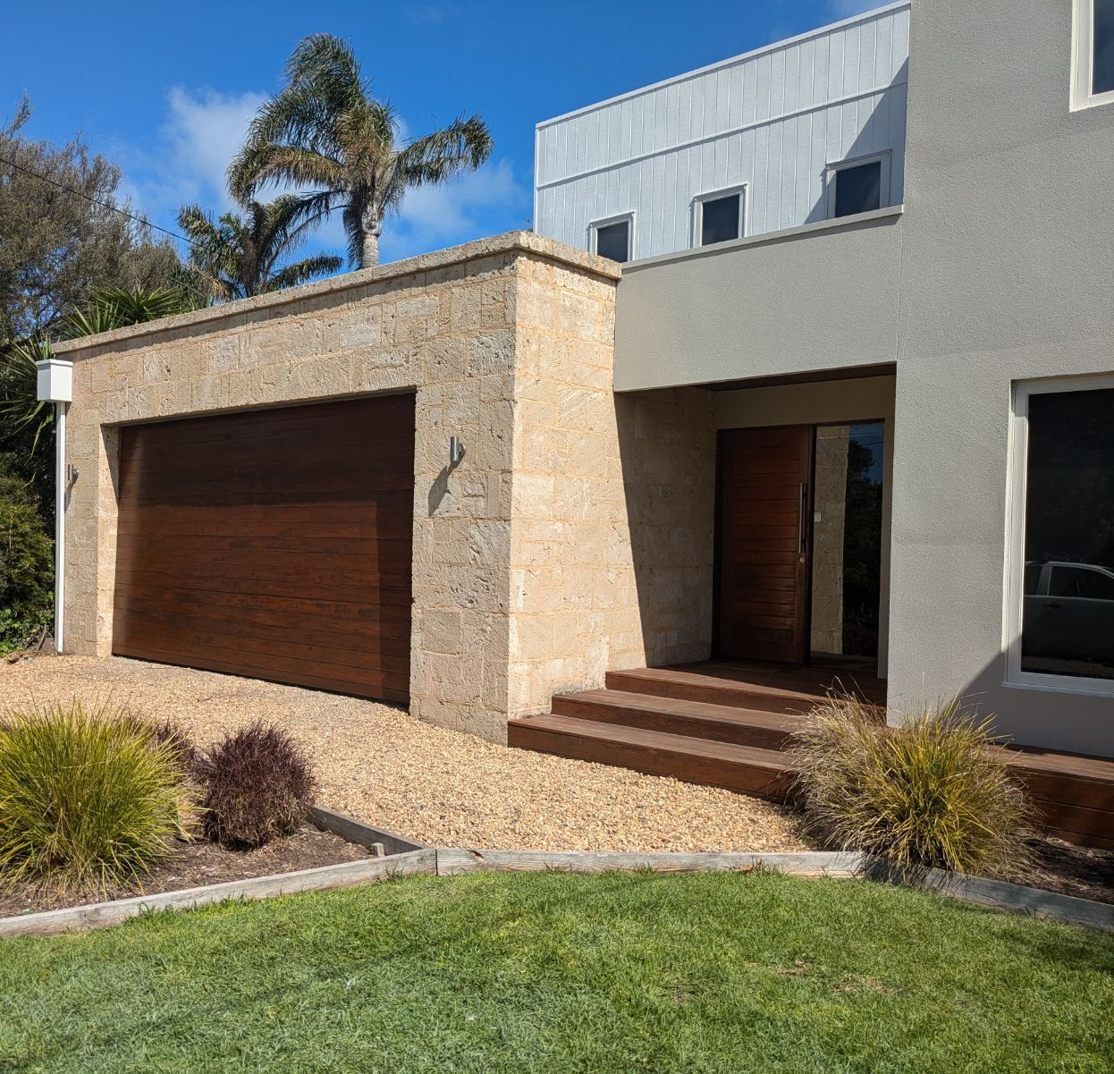 Modern house exterior with stone garage, wooden door, steps, and landscaped lawn