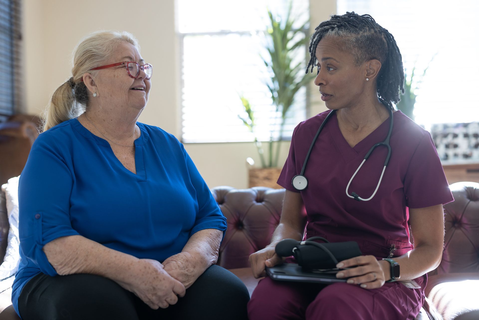 A nurse is talking to an older woman while sitting on a couch.