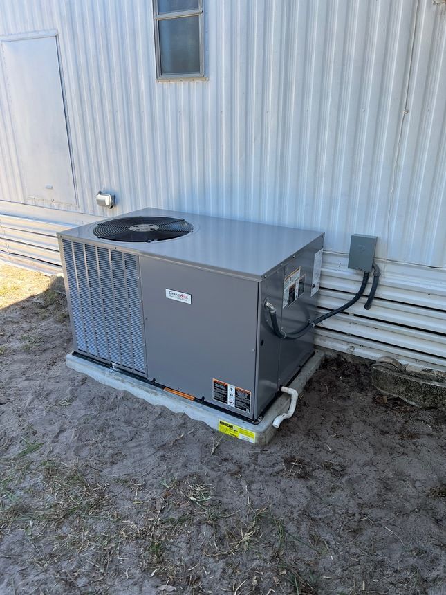 An outdoor air conditioning unit on a concrete pad next to a white wall.