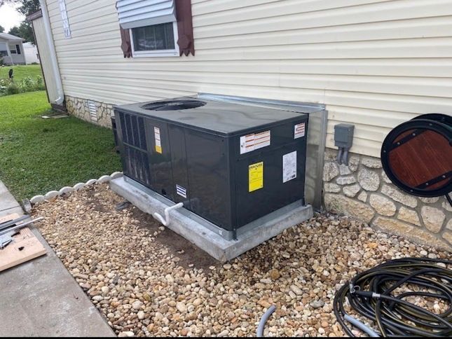 New air conditioning unit outside a light-colored building, sitting on a concrete pad surrounded by gravel.