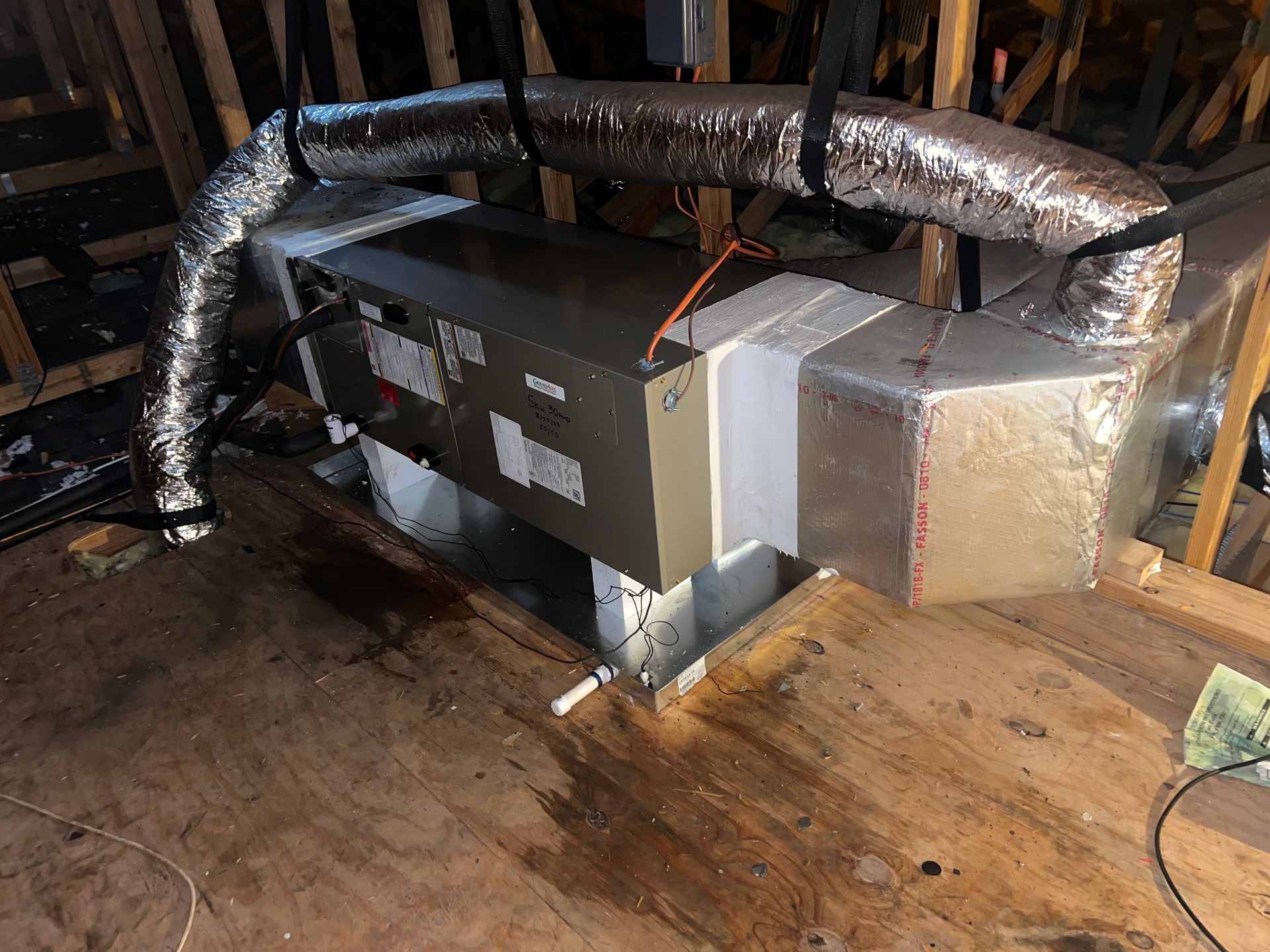 HVAC unit in an attic. Ductwork connected to a metal air handler. Wooden floor.