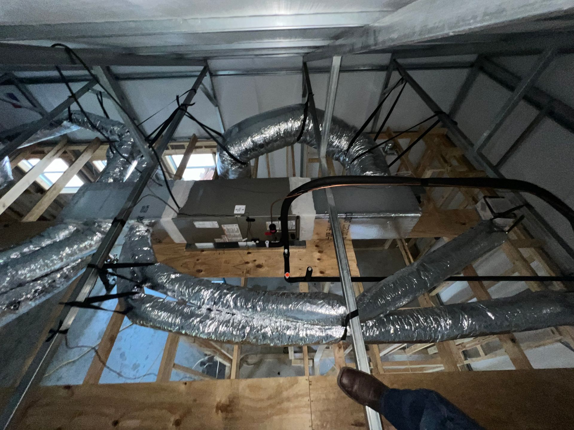 Interior attic view with HVAC system and ductwork installed. Silver ducting against exposed wood framing.
