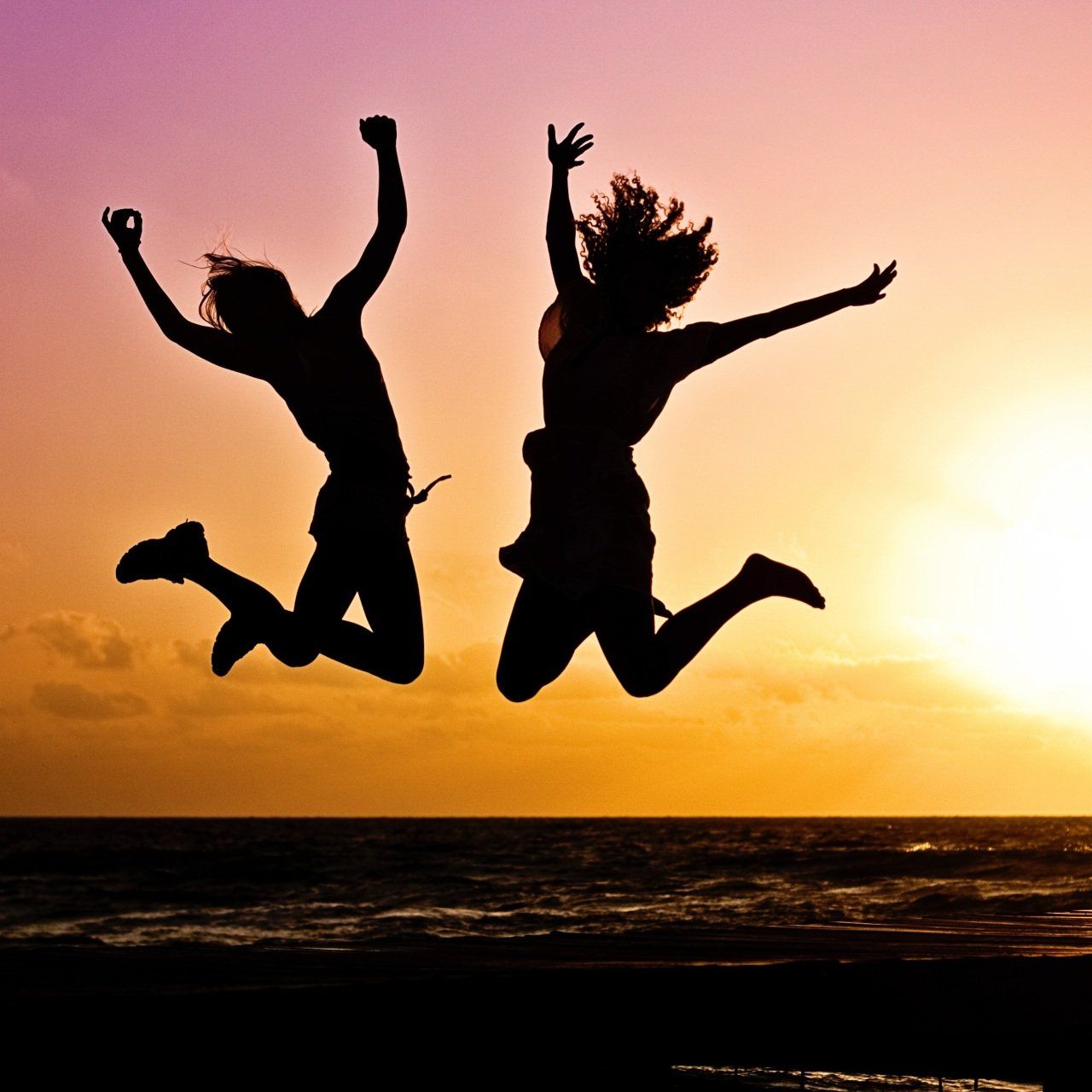 Two people are jumping in the air at sunset
