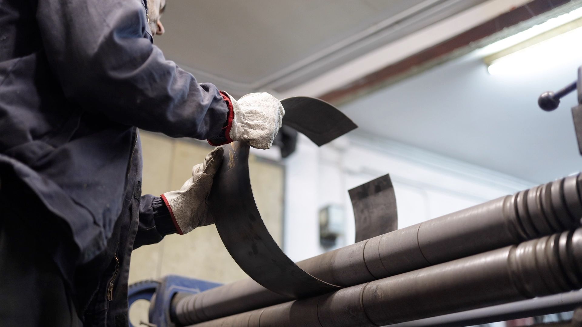 Worker in gloves handling a black curved tool beside metal pipes in an industrial setting Worker in gloves handling a black curved tool beside metal pipes in an industrial setting