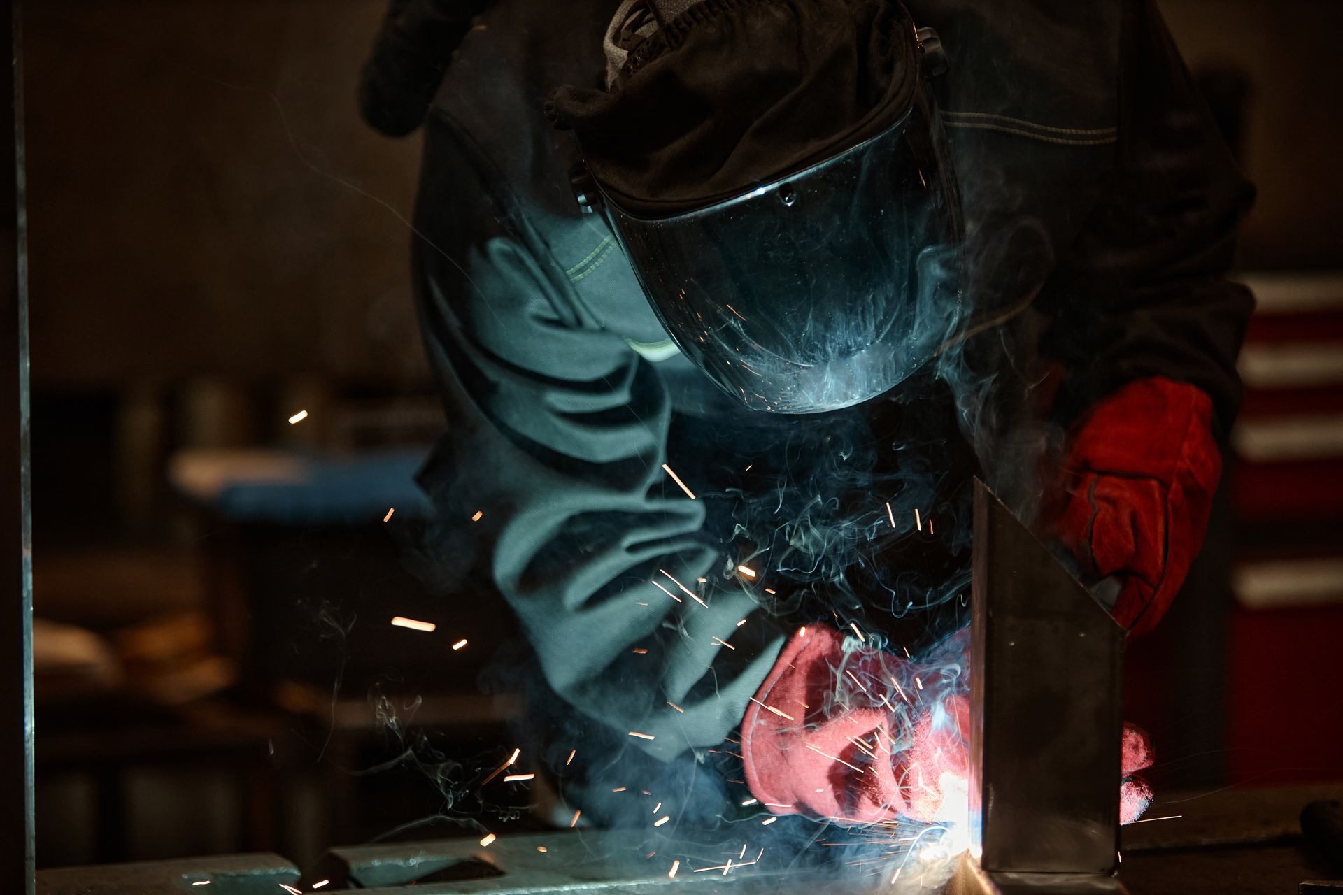 Person welding metal with bright sparks in a dark workshop, wearing protective gear and red gloves Person welding metal with bright sparks in a dark workshop, wearing protective gear and red gloves